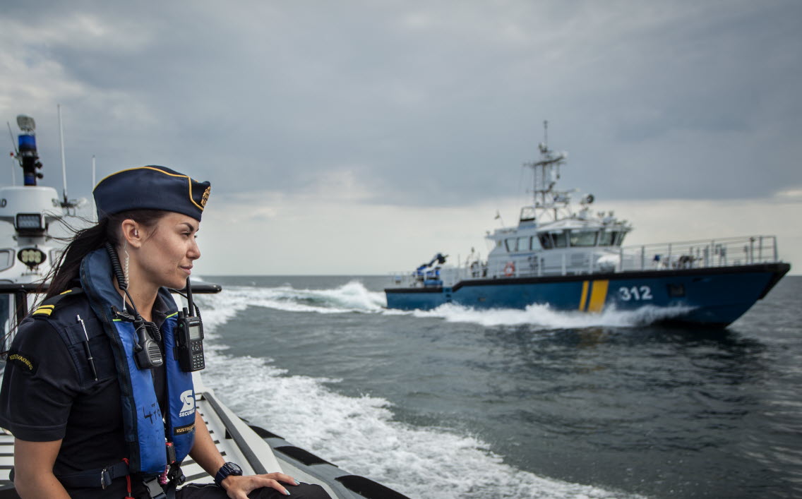 Kvinnlig kustbevakare på fartyg med KBV 312 i bakgrunden.